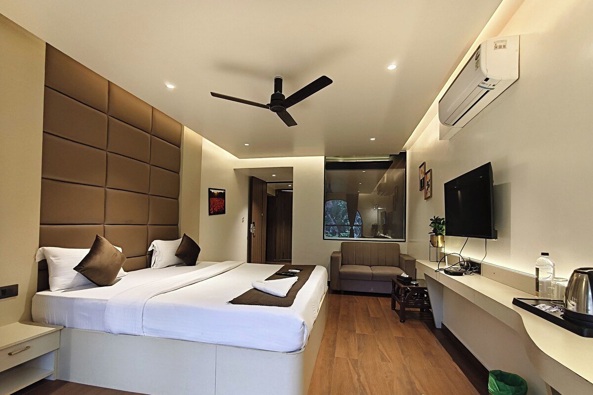 A modern hotel room with a large bed, a sofa, a TV, and a desk.