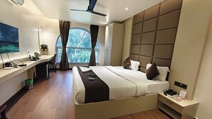Una habitación de hotel moderna con una cama grande, un escritorio y vistas a zonas verdes a través de una ventana.