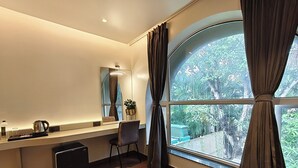 Una habitación moderna con un ventanal grande, un escritorio con hervidor, una silla y una pequeña planta en maceta.