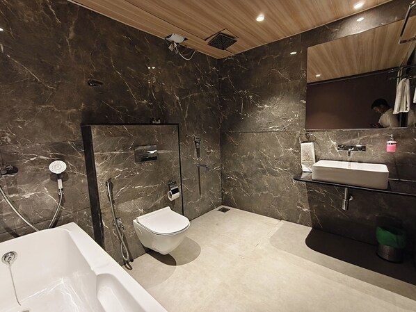 Un baño moderno con bañera, inodoro y zona de ducha, que cuenta con paredes de mármol y techo de madera.