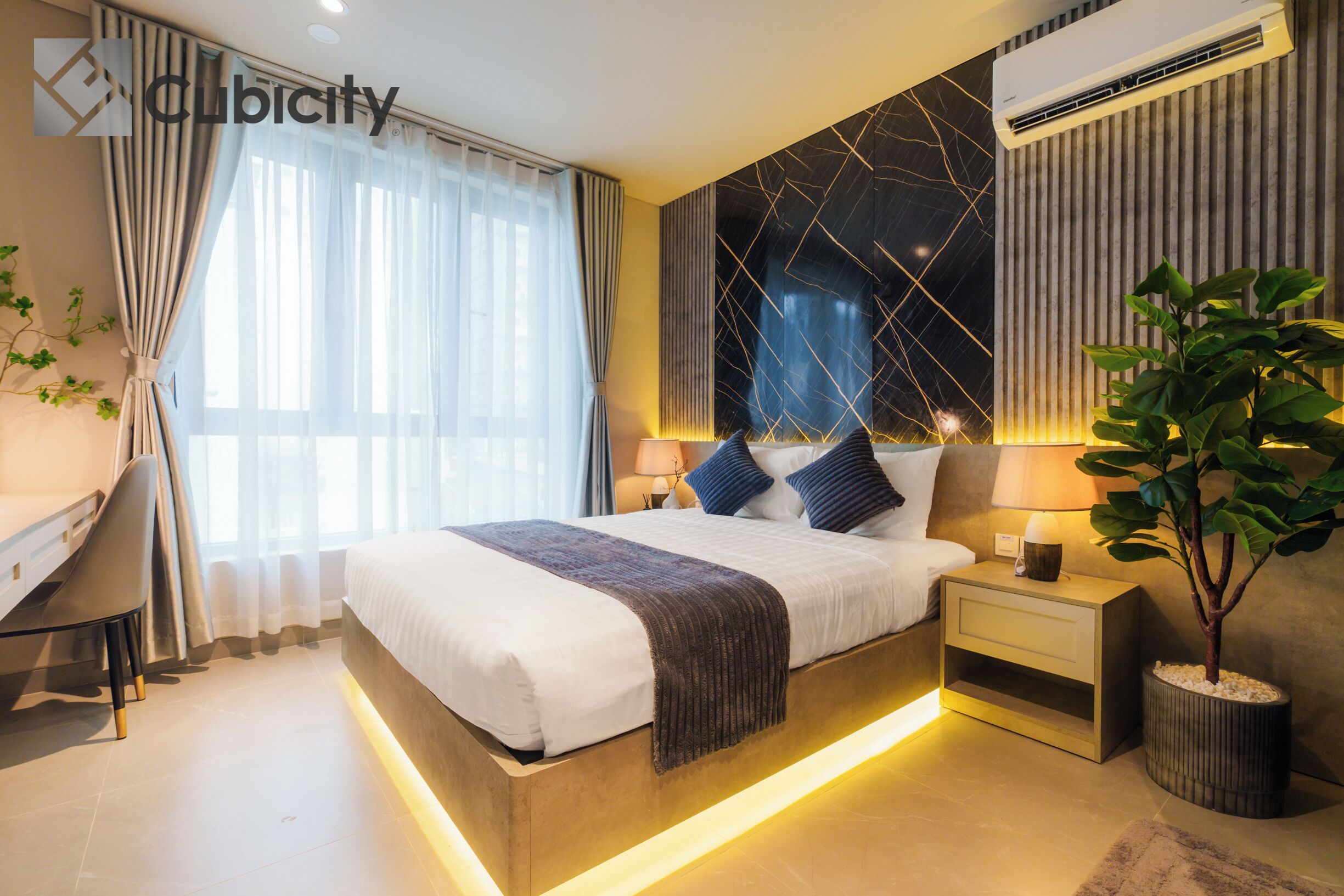 A modern hotel room with a large bed, bedside tables, a desk, and a potted plant.