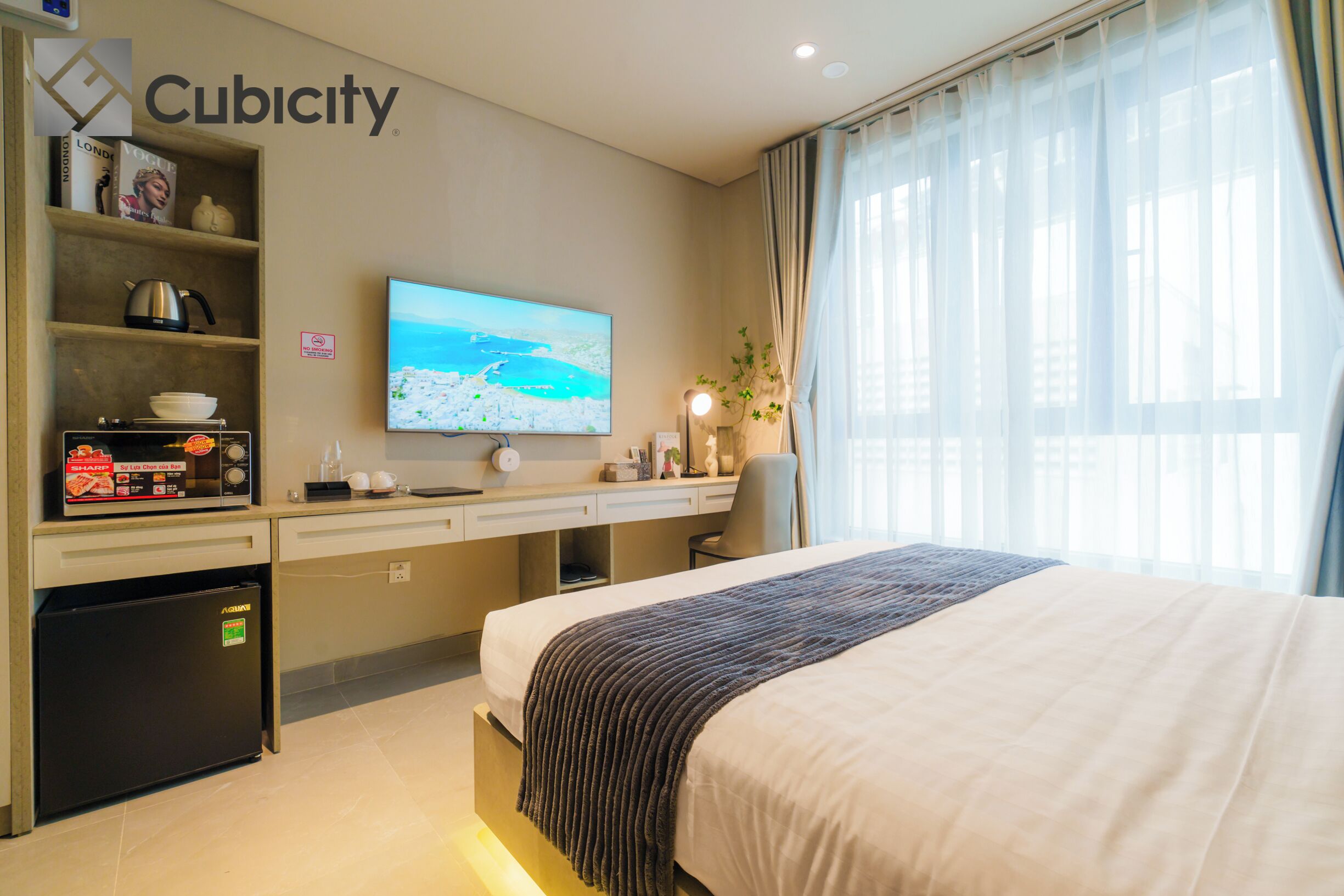A hotel room with a bed, a desk with a computer, a television, and a refrigerator.