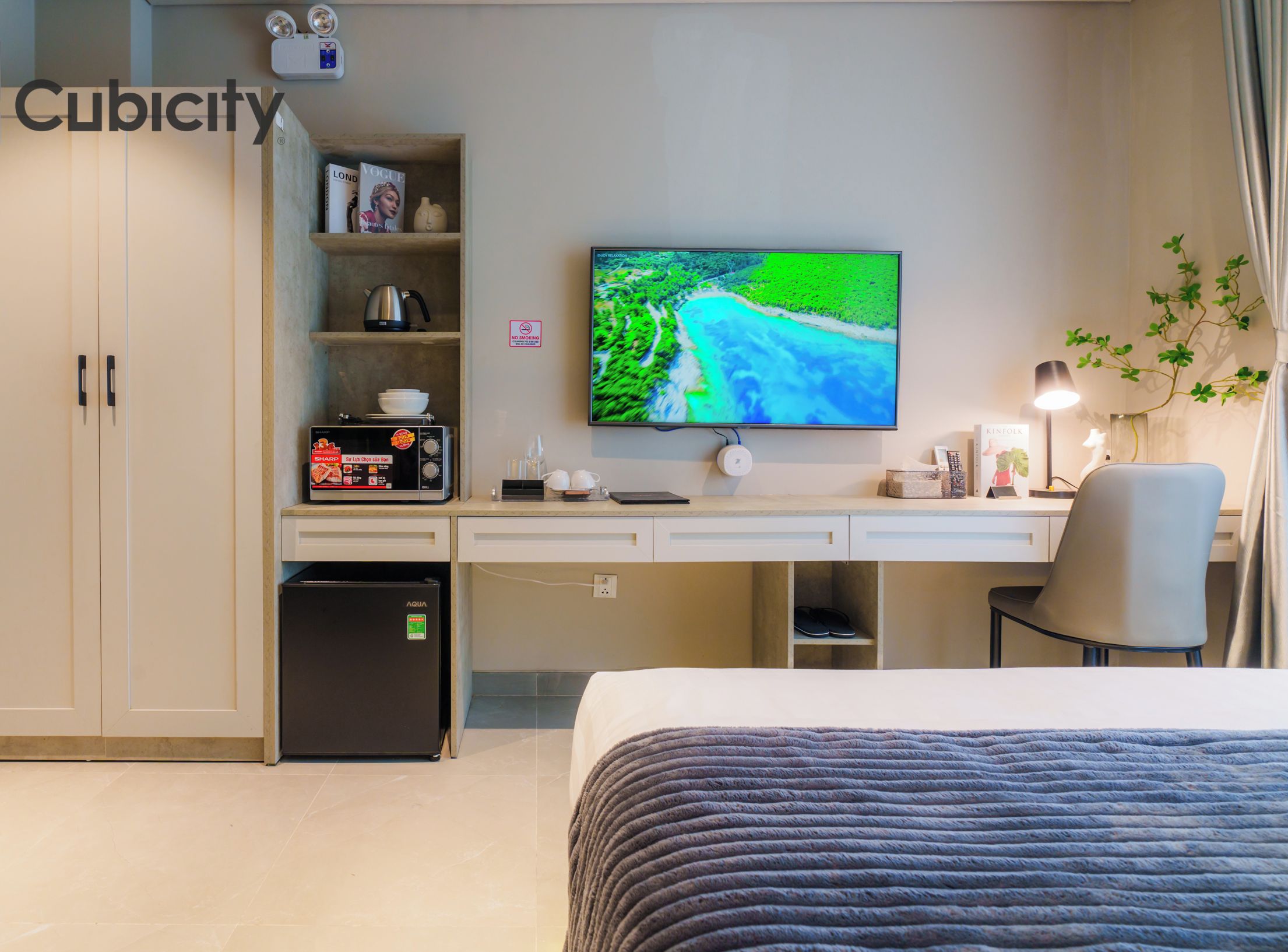 A hotel room with a bed, a desk with a computer, a television, and a minibar.