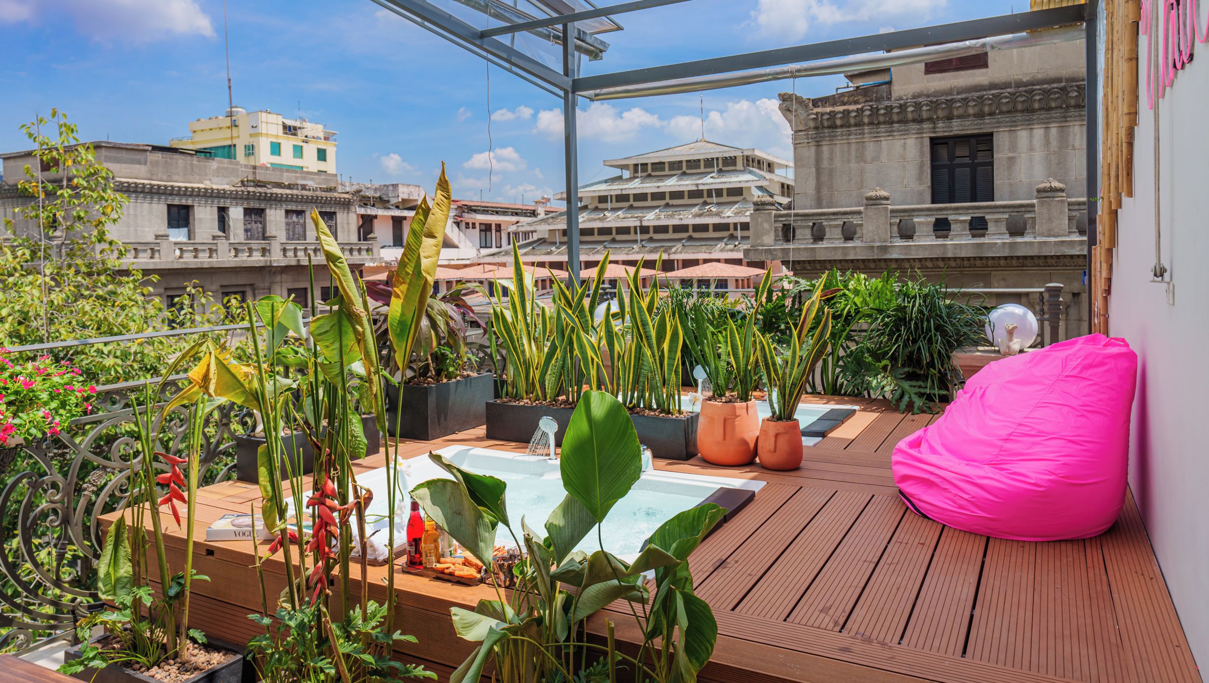 Une terrasse sur le toit agrémentée de plantes en pot, d’un jacuzzi et d’un fauteuil en forme de haricot rose.
