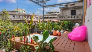 Een terras op het dak met plantenpotten, een jacuzzi en een roze loungestoel.