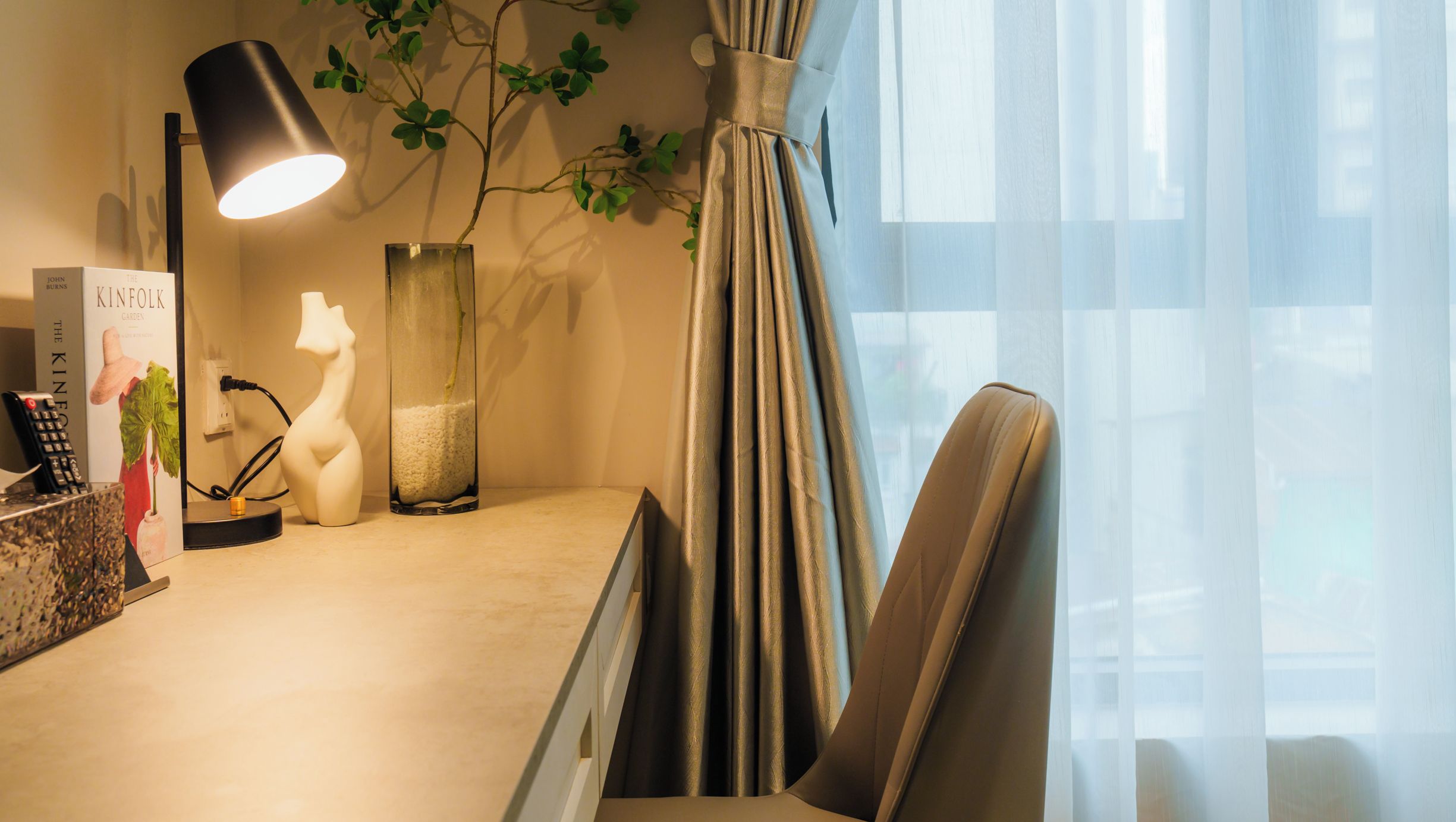 Une chambre d’hôtel équipée d’un bureau, d’une lampe, d’objets décoratifs et de rideaux en voile.