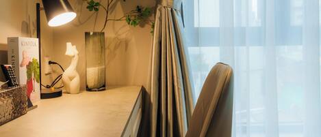 Una habitación de hotel con escritorio, lámpara, adornos y cortinas traslúcidas.