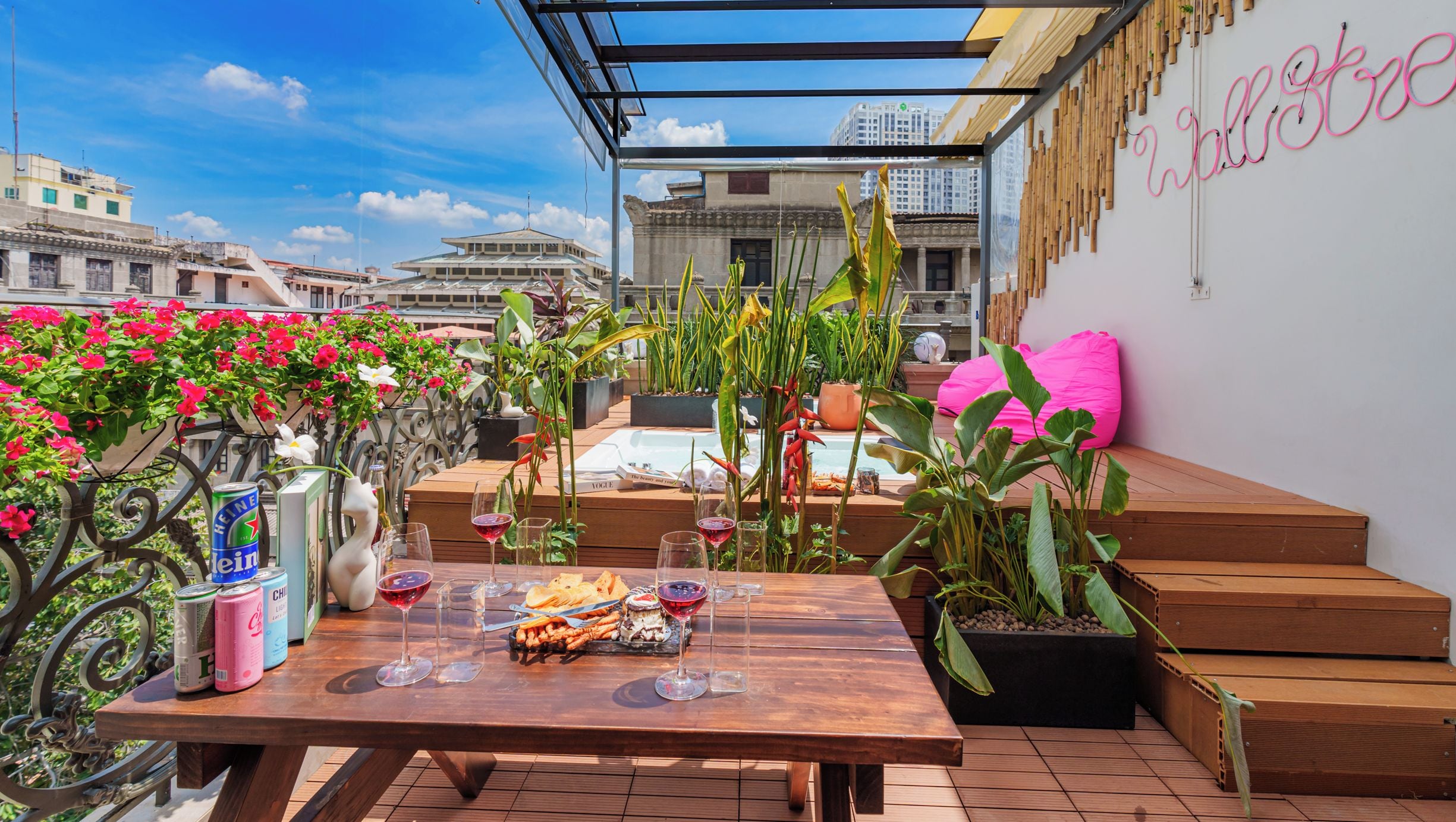 Une terrasse extérieure avec une table en bois dressée pour le repas, entourée de plantes en pot et offrant une vue sur la ville.