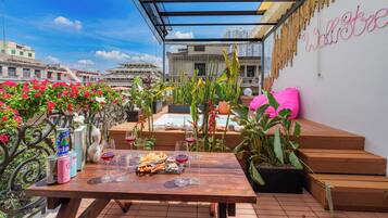 Une terrasse extérieure avec une table en bois dressée pour le repas, entourée de plantes en pot et offrant une vue sur la ville.