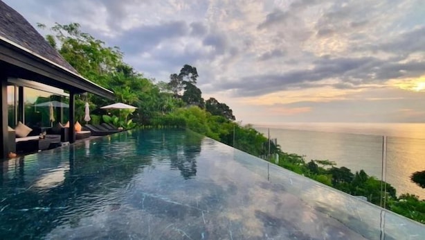 A infinity pool with a view of the sea, surrounded by lush greenery and a covered seating area with umbrellas.