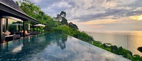 An infinity pool with a view of the sea and a building with outdoor seating.