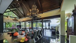 A modern dining area with a long table, chairs, and a chandelier.