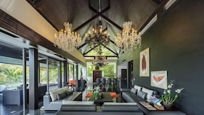 A modern living room with a high ceiling, large windows, and a chandelier.