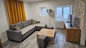 Una sala de estar con un sofá seccional gris, una mesa de centro de madera, un pequeño otoman, una lámpara y una pared de piedra.