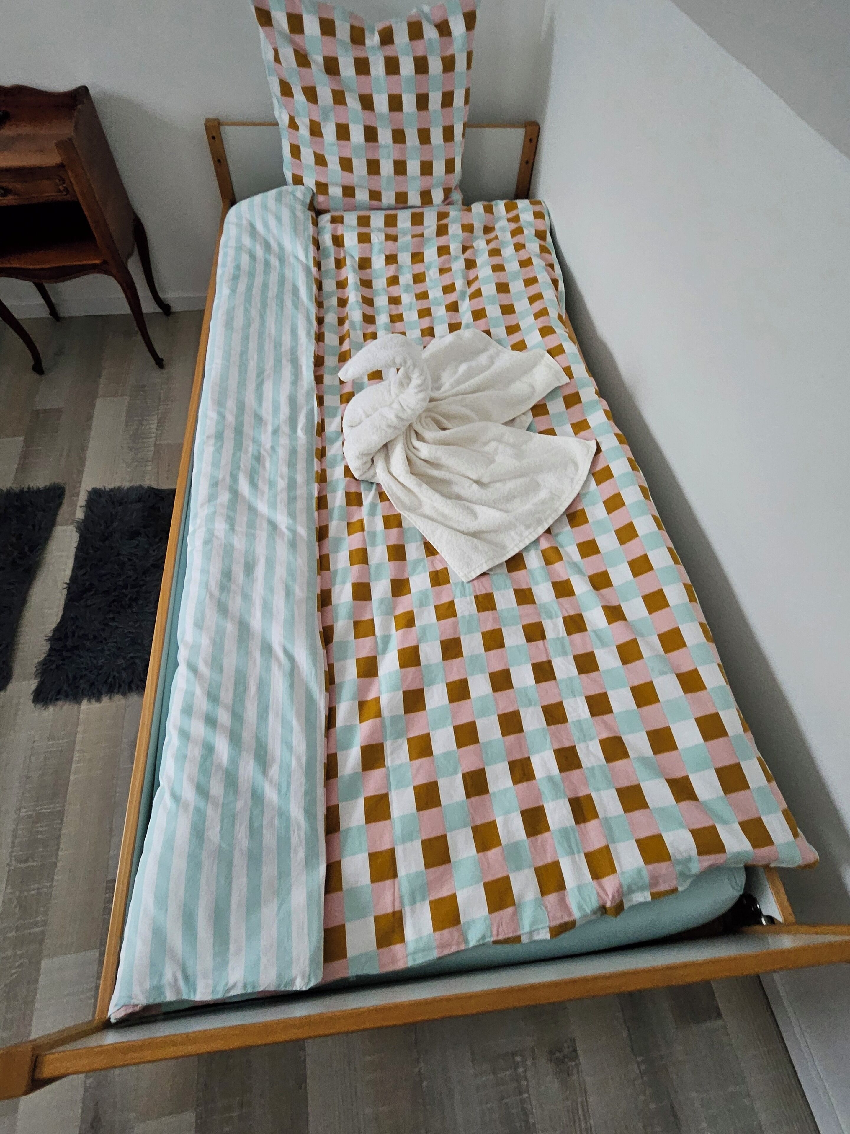 Un lit simple avec une couvre-lit à carreaux, un oreiller rayé et une serviette.