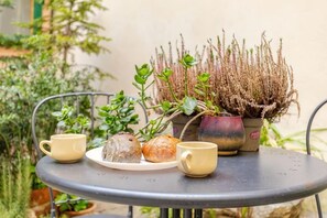 A round metal table with two yellow cups and a plate with two pastries, accompanied by a potted plant with green foliage and a taller plant with brown, spiky leaves. - Vintage apartments in the center of Florence (Florence)
