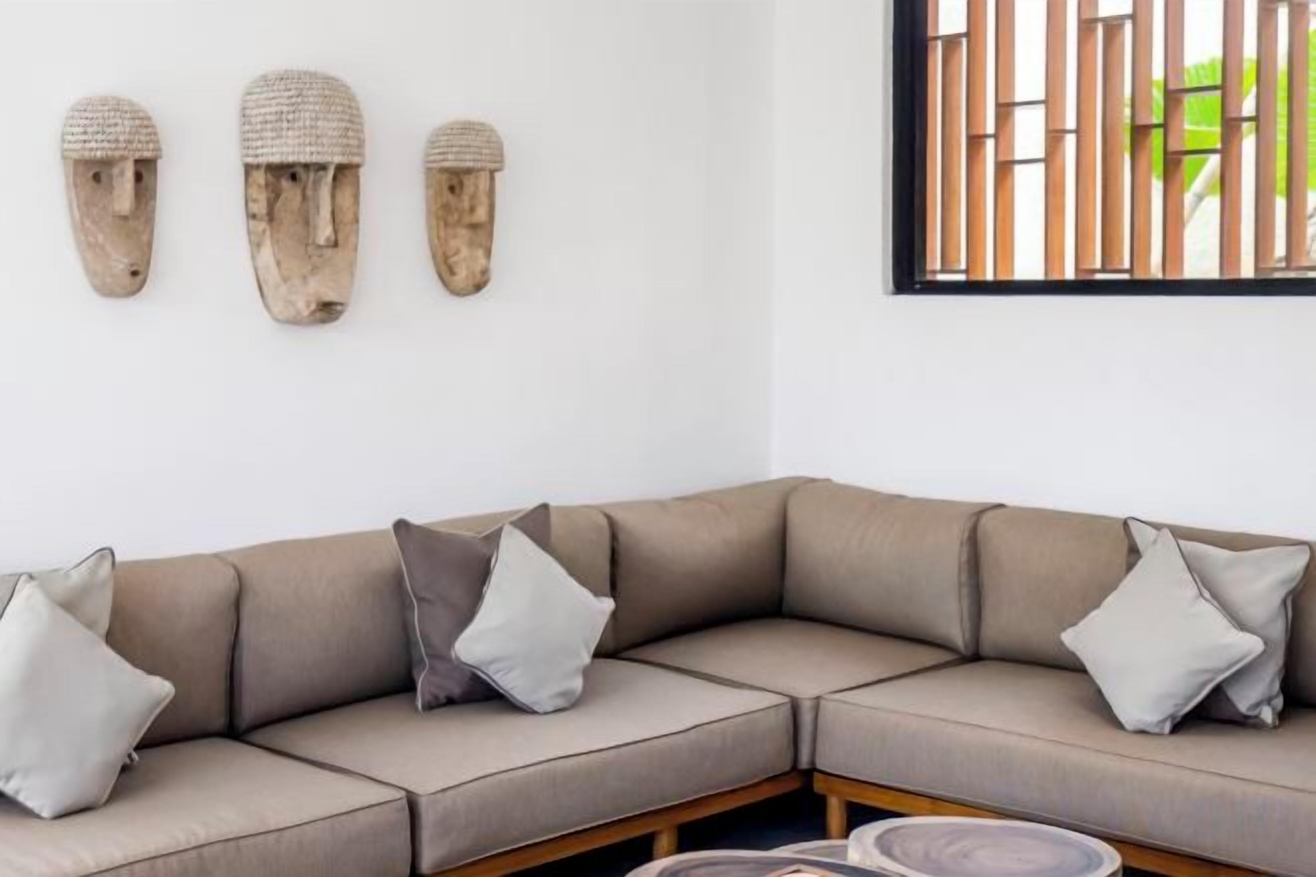 A modern living room with a beige sectional sofa, three cushions, and three woven wall art pieces.