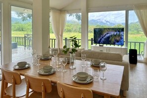 A dining area with a table set for six, a sofa, and a television screen displaying a mountainous landscape. - Khaoyai Valley8 (3BR-max 10 guests) (Pak Chong)