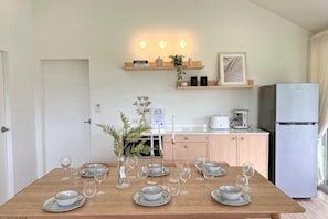 A dining table set with plates and glasses, a refrigerator, a coffee maker, and a plant on a shelf. - Khaoyai Valley8 (3BR-max 10 guests) (Pak Chong)