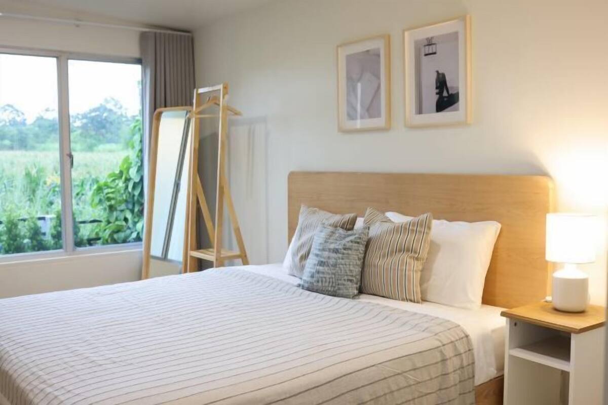 A neatly made bed with striped bedding, a bedside table with a lamp, and two framed pictures on the wall.