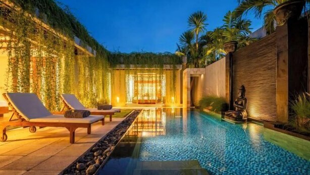 A serene outdoor pool area with lounge chairs and a statue, surrounded by lush greenery and palm trees.