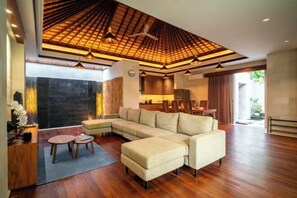 A modern living room with a sectional sofa, a wooden ceiling, and a dining area. - Bali KBS Villas at Jimbaran Bay (Bali)