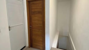 A narrow hallway with a white door on the left and a wooden door on the right. - Home Stay Room In Bali (Bali)