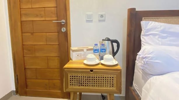 A wooden door, a bedside table with a kettle, and a bed with white linens. - Home Stay Room In Bali (Bali)