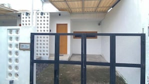 A gated courtyard with a metal gate, a wooden door, and a small window. - Home Stay Room In Bali (Bali)