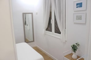 A small, clean room with a single bed, a window with curtains, a mirror, and a small table with a plant. - NEW, CENTRAL NEAR BEACH AND SEA by www.SanSebastianApartments.es (San Sebastian)