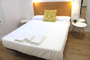 A neatly made bed with white linens and a green pillow, a small round table, and a mirror on the wall. - NEW, CENTRAL NEAR BEACH AND SEA by www.SanSebastianApartments.es (San Sebastian)