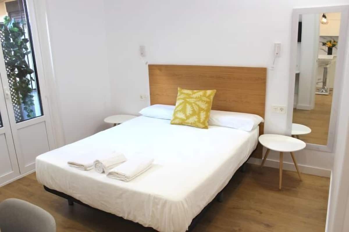 A neatly made bed with a wooden headboard, white bedding, and a yellow pillow. There are two small white side tables and a chair in the room.