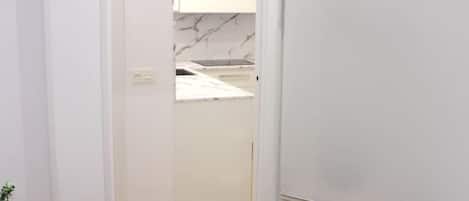 A hallway leading to a kitchen with white cabinets and a marble backsplash.