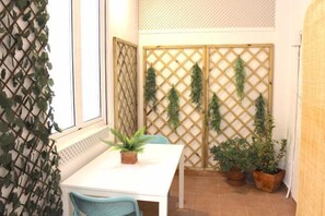 Een kleine eethoek met een witte tafel en blauwe stoelen, omgeven door potplanten en een houten lattenwand.
