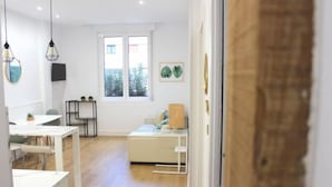 A modern, well-lit room with a wooden floor, a white sofa, a small table, and a window with a view of greenery outside. - NEW, CENTRAL NEAR BEACH AND SEA by www.SanSebastianApartments.es (San Sebastian)