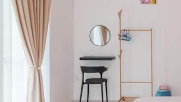 A bedroom with a bed, a desk with a chair, a mirror, a coat rack, and a small shelf.