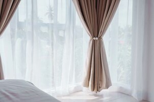 Un dormitorio con cama, cortinas translúcidas y vistas a palmeras.