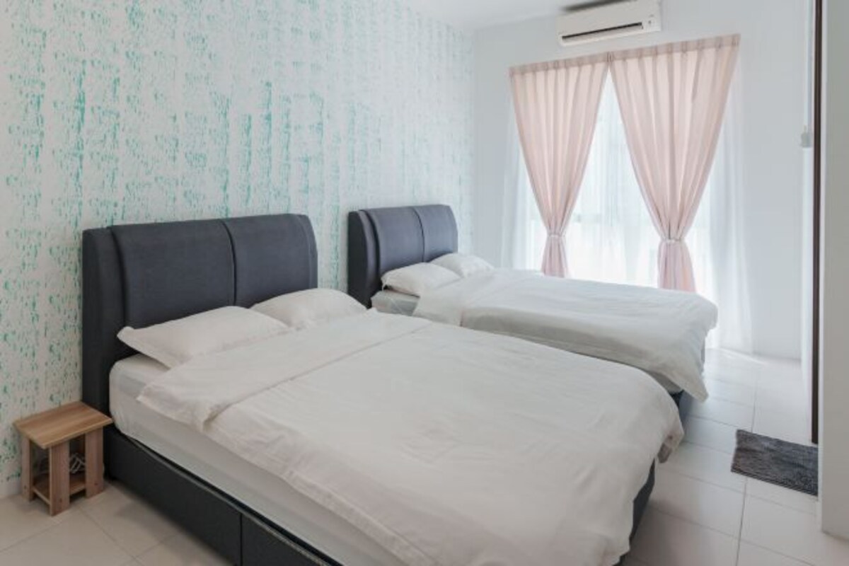A bedroom with two beds, a small wooden stool, and a window with sheer curtains.