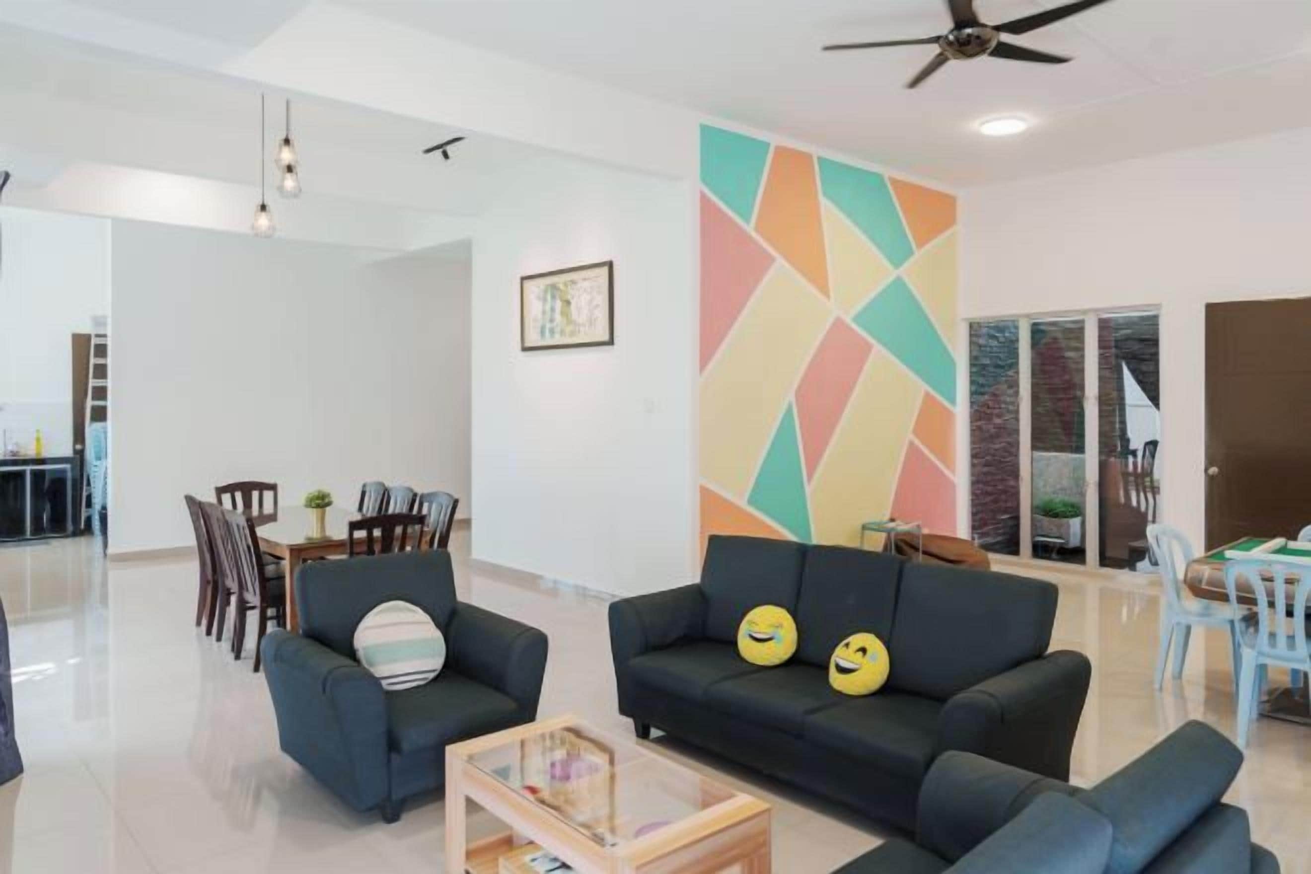 A modern living room with a sofa, armchairs, and a coffee table. There is a colorful geometric wall art and a ceiling fan.