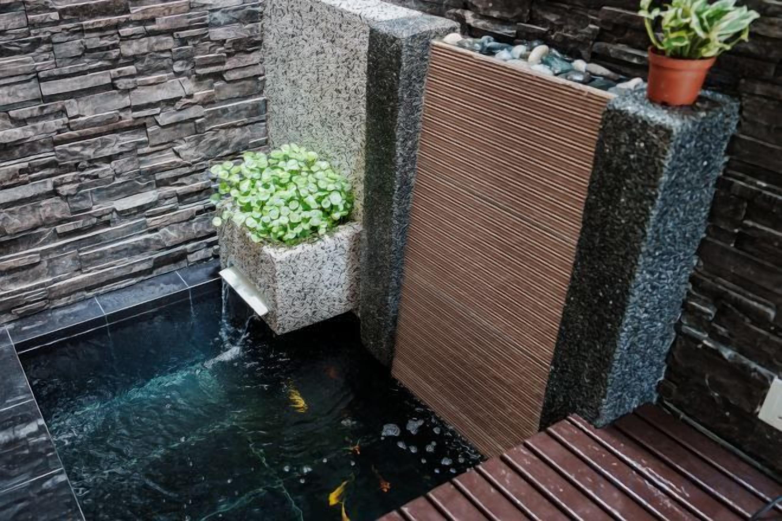 Un élément décoratif aquatique avec une petite cascade, un bac à plantes orné de feuillage verdoyant et un panneau vertical à texture.