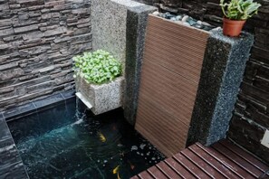 A water feature with a small waterfall, a planter with green foliage, and a textured vertical panel. - Secret Garden Homestay (Kuala Selangor)