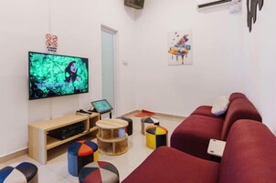 Una sala de estar con televisor, sofá, mesa de centro y una mesita con una computadora portátil.
