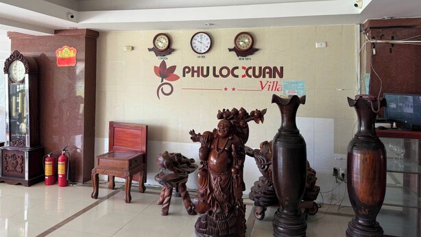A lobby with a clock displaying London time, a wooden statue, and a sign reading "PHU LOC XUAN Village". - OYO 1296 Phu Loc Xuan Hotel Danang (Da Nang)