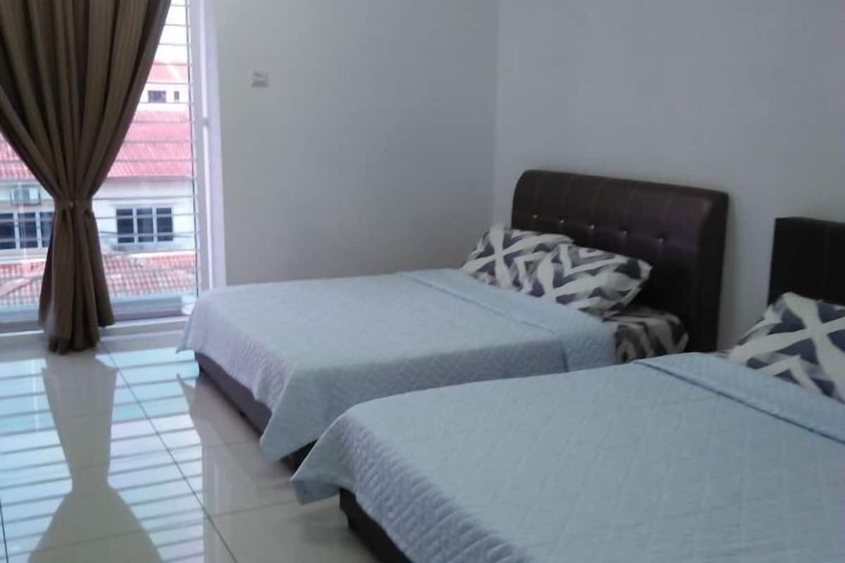 A hotel room with two beds, a window with curtains, and a view of buildings outside.