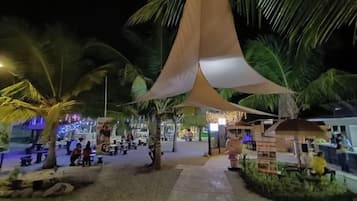 An outdoor area with palm trees, a shaded seating area, and a pathway leading to a building.
