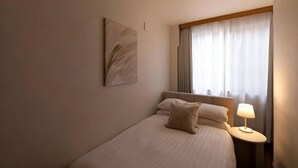 A hotel room with a bed, a bedside table with a lamp, a window with curtains, and a wall-mounted artwork. - Tsutenkaku Royal House - Self Check-In Only (Osaka)