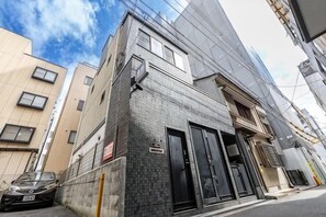 A multi-story building with a tiled facade, a black entrance door, and a visible parking area. - Tsutenkaku Royal House - Self Check-In Only (Osaka)