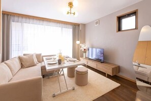 A modern living room with a sofa, a TV, a dining table, and a small cabinet. - Tsutenkaku Royal House - Self Check-In Only (Osaka)