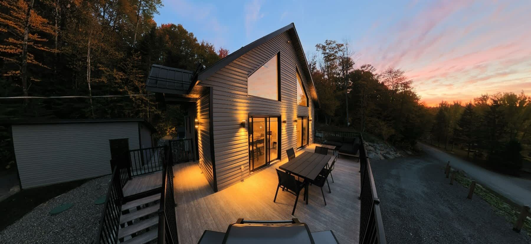 A modern house with a deck, large windows, and a view of the surrounding forest.