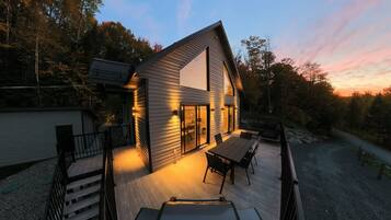 A modern house with a deck, large windows, and a view of the surrounding forest.